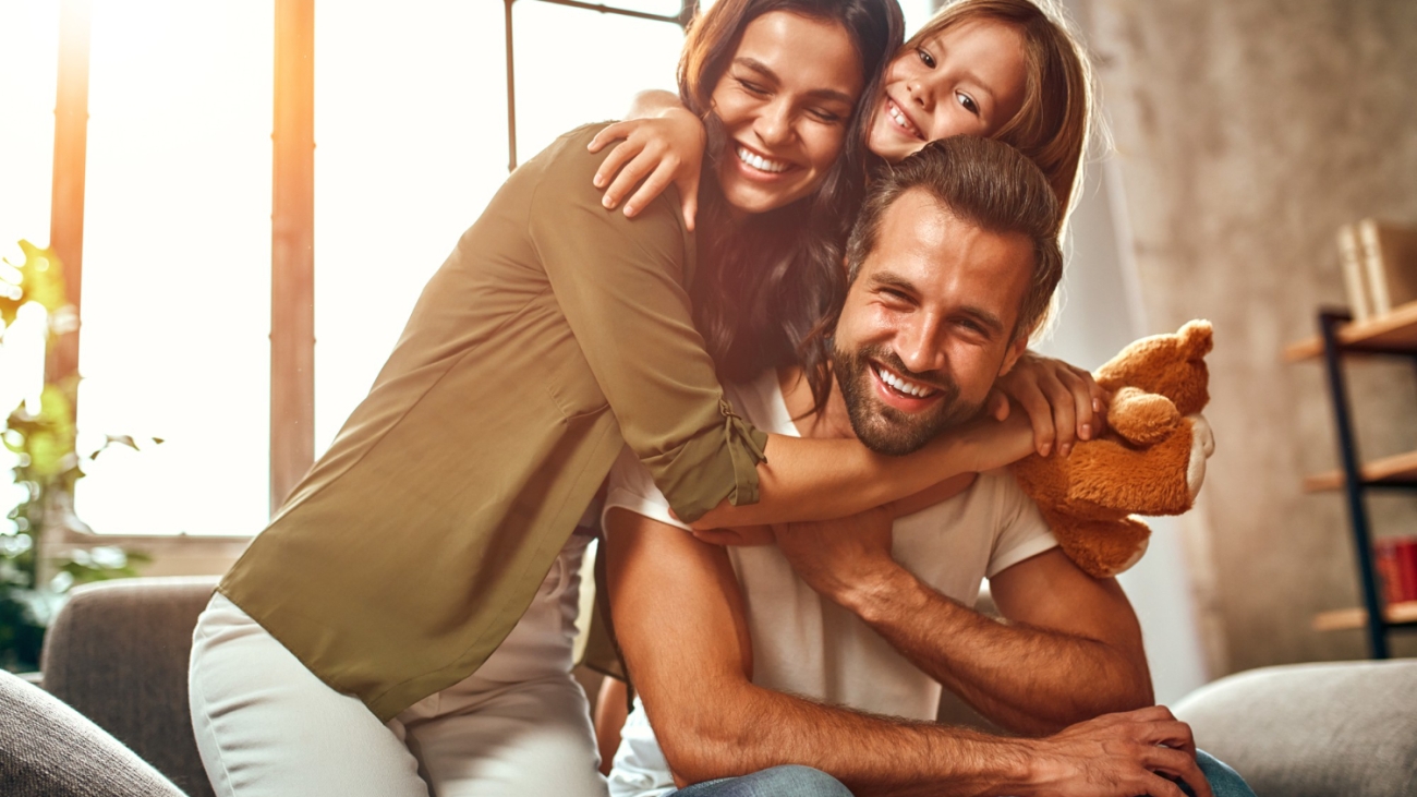happy-dad-mom-with-their-cute-daughter-teddy-bear-hug-have-fun-sitting-sofa-living-room-home